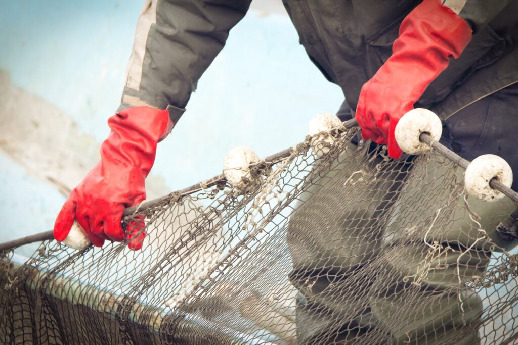 Person wearing red gloves holds a fishing net with white floats, preparing or inspecting it.