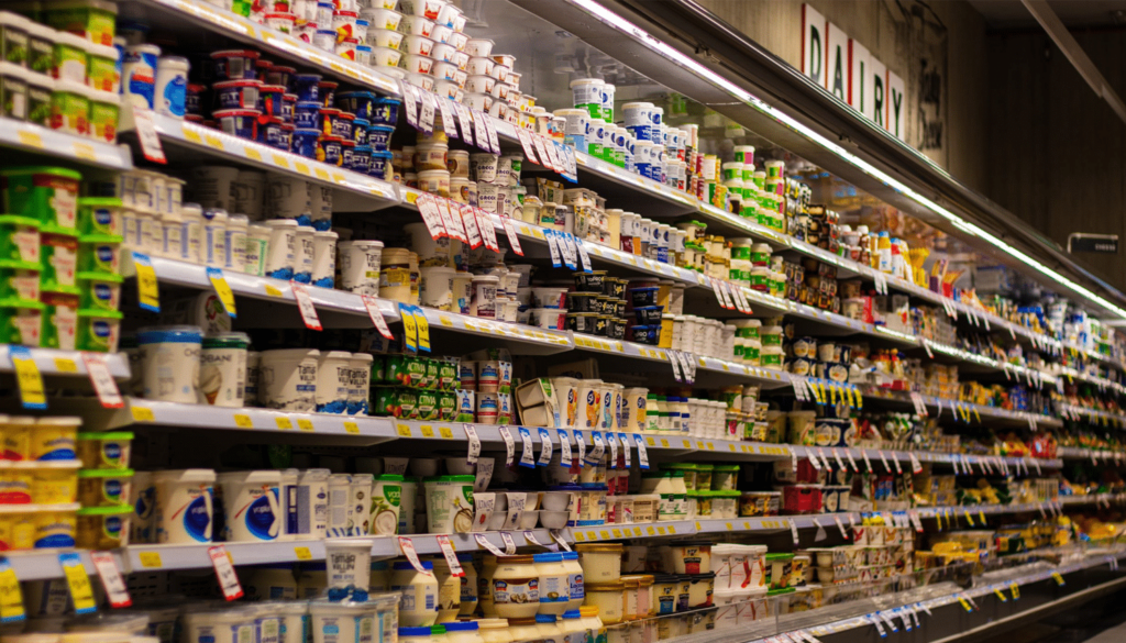 Shelves in a grocery store refrigerator section stocked with various dairy products such as yogurt, butter, and cheese.