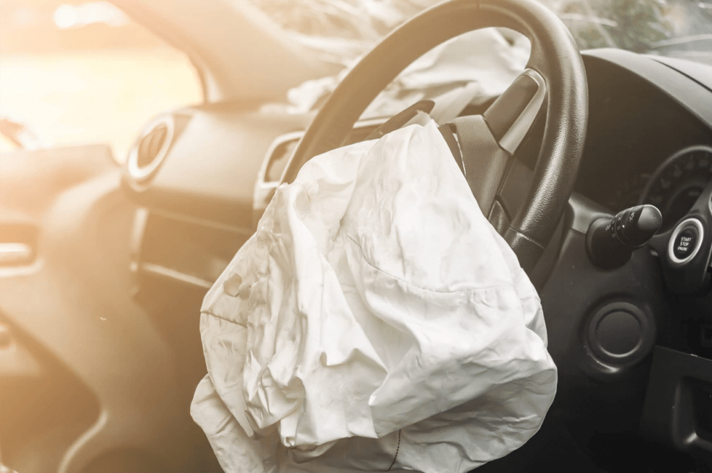 Deployed airbag inside a car with sunlight shining through the window, indicating a recent impact or collision.