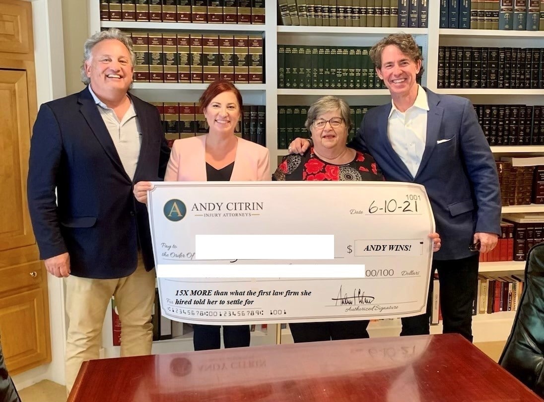 Four people stand in a law office holding a large ceremonial check from Andy Citrin Injury Attorneys, dated 6-10-21. Bookshelves filled with legal books are in the background.