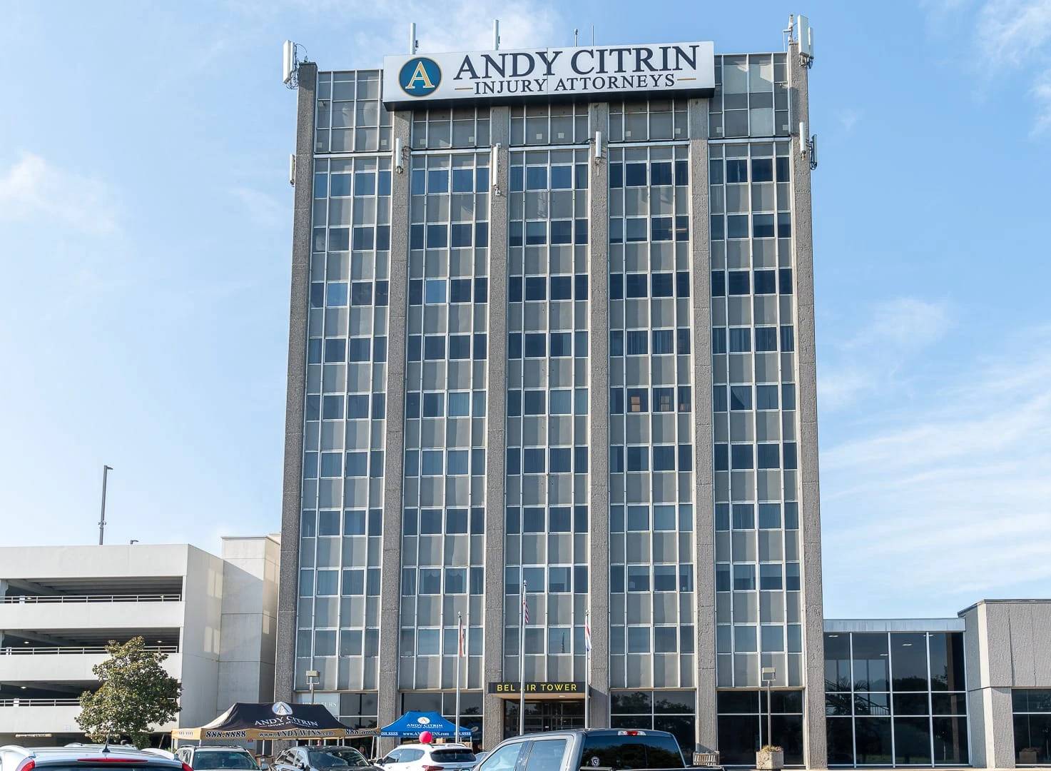 Tall office building with a sign reading “Andy Citrin Injury Attorneys” at the top, with a few cars and tents visible in the parking lot in front.