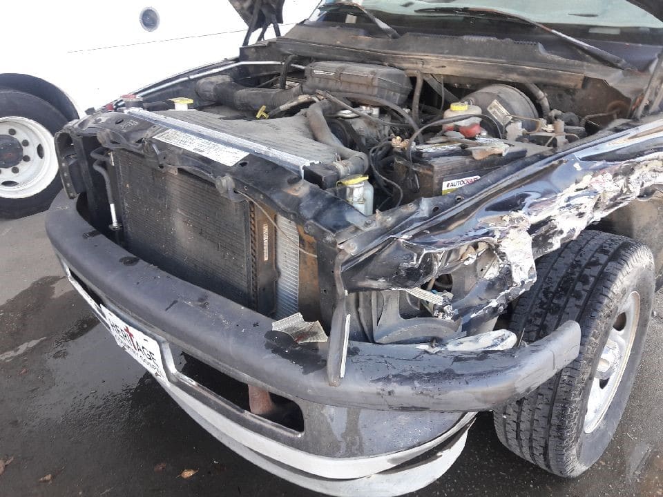 A black pickup truck with significant front-end damage, exposing the engine and radiator, with a bent bumper and crumpled hood.