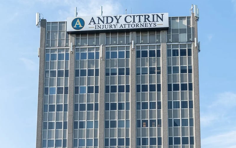 A tall office building with a sign at the top reading "Andy Citrin Injury Attorneys" against a blue sky.